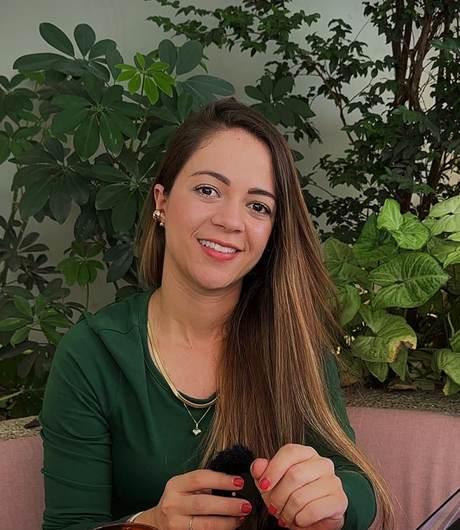 Flor Diez sonriendo, sentada en una mesa de madera con plantas detrás